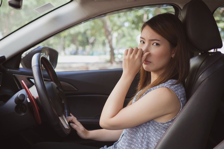 Woman in car holding nose because her car stinks